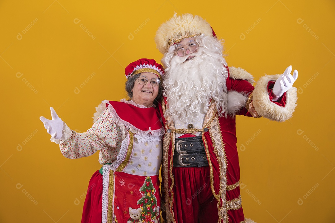 Lindo Casal Papai Noel ao lado de Mamãe Noel sobre fundo isolado amarelo