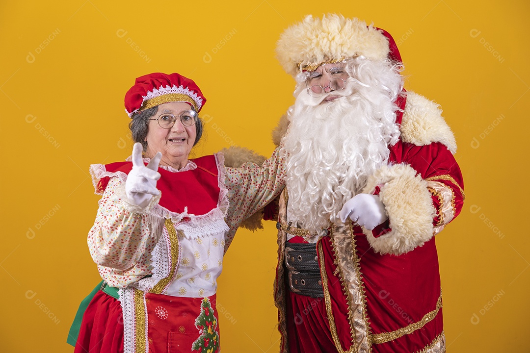 Lindo Casal Papai Noel ao lado de Mamãe Noel sobre fundo isolado amarelo