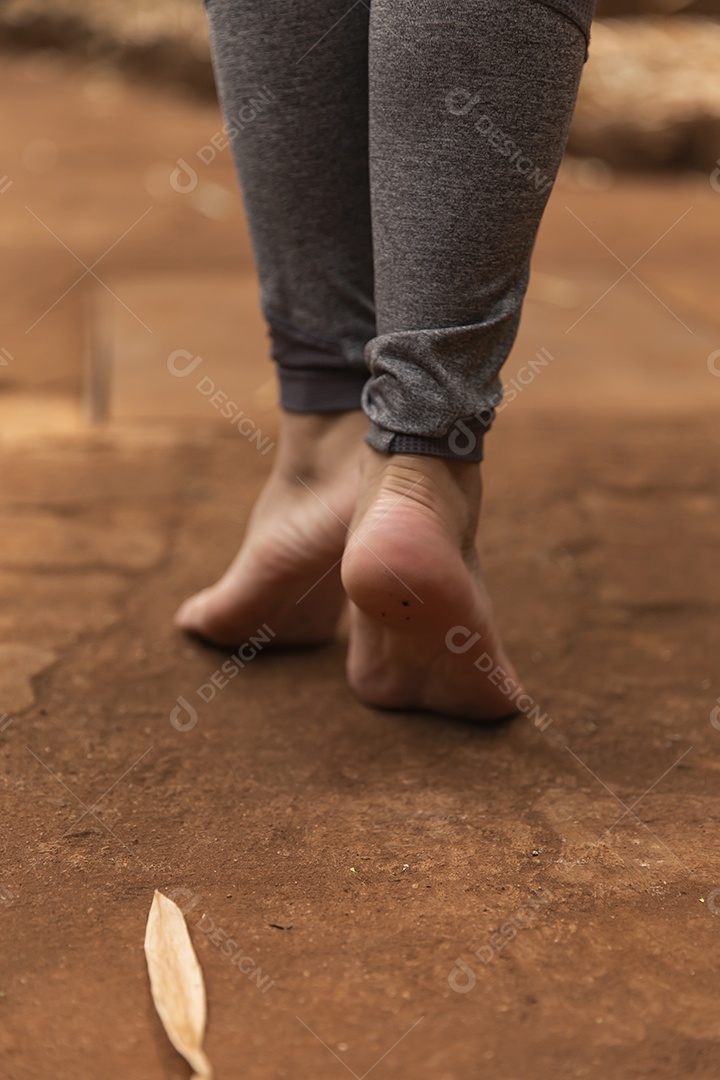 Pés de pessoa andando sobre chão de terra