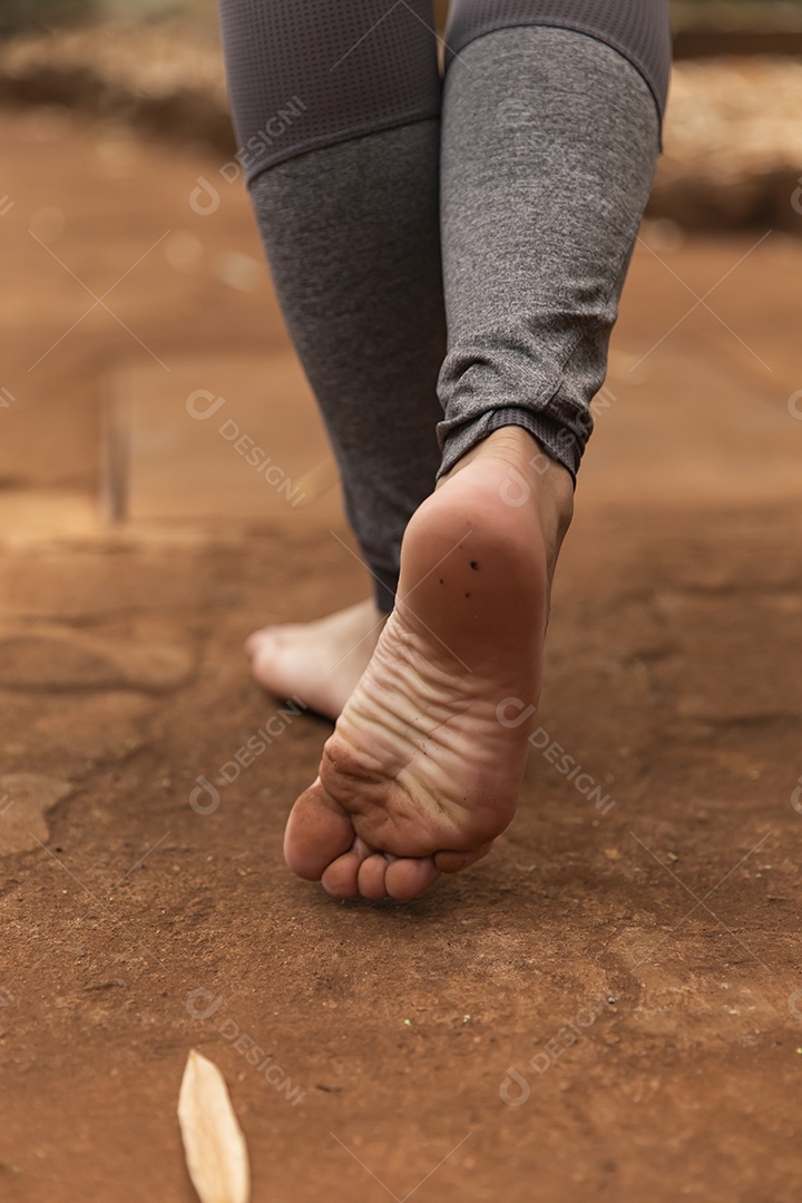 Pés de pessoa andando sobre chão de terra