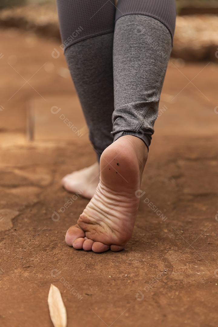 Pés de pessoa andando sobre chão de terra