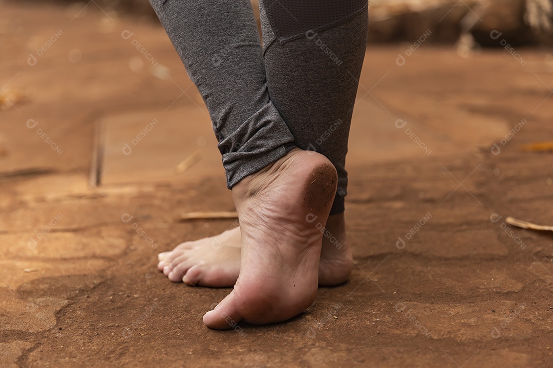 Pés de pessoa andando sobre chão de terra
