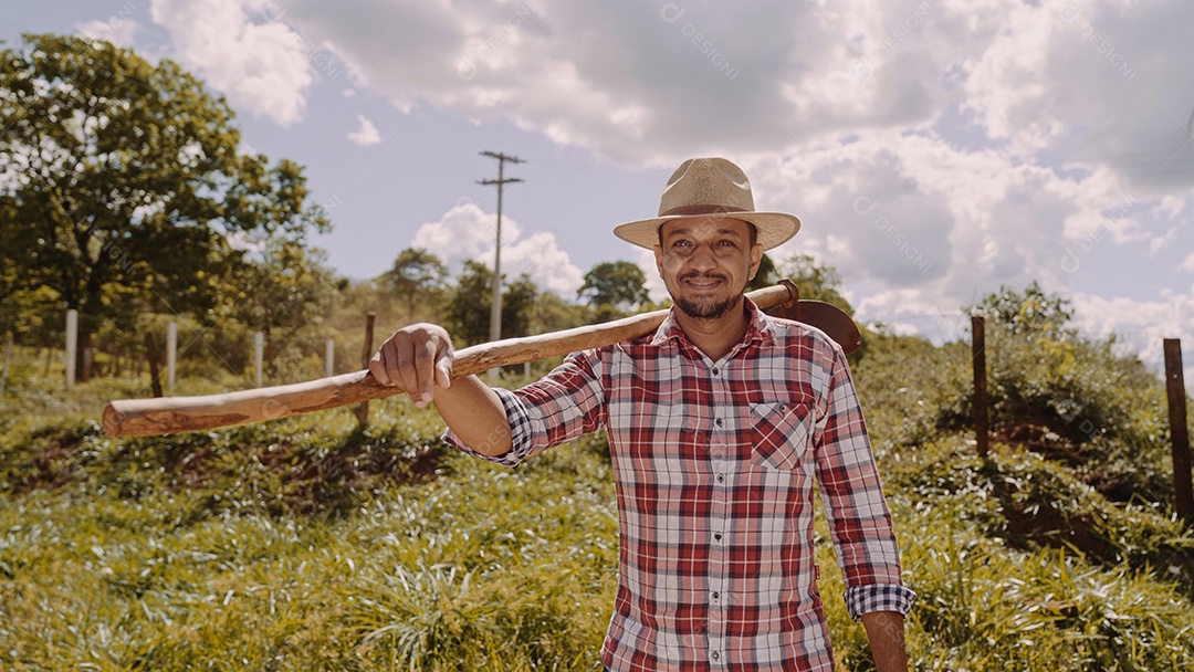 Homem meia idade agricultor com uma inchada no seu ombro sobre fazenda