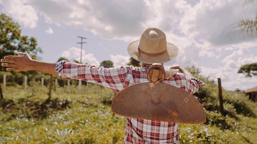 Homem meia idade agricultor com uma inchada no seu ombro sobre fazenda