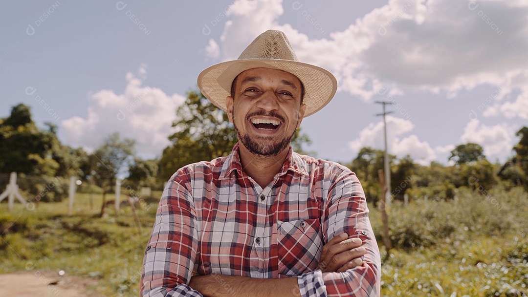 Retrato de jovem agricultor com mãos cruzadas na camisa casual e chapéu na fazenda