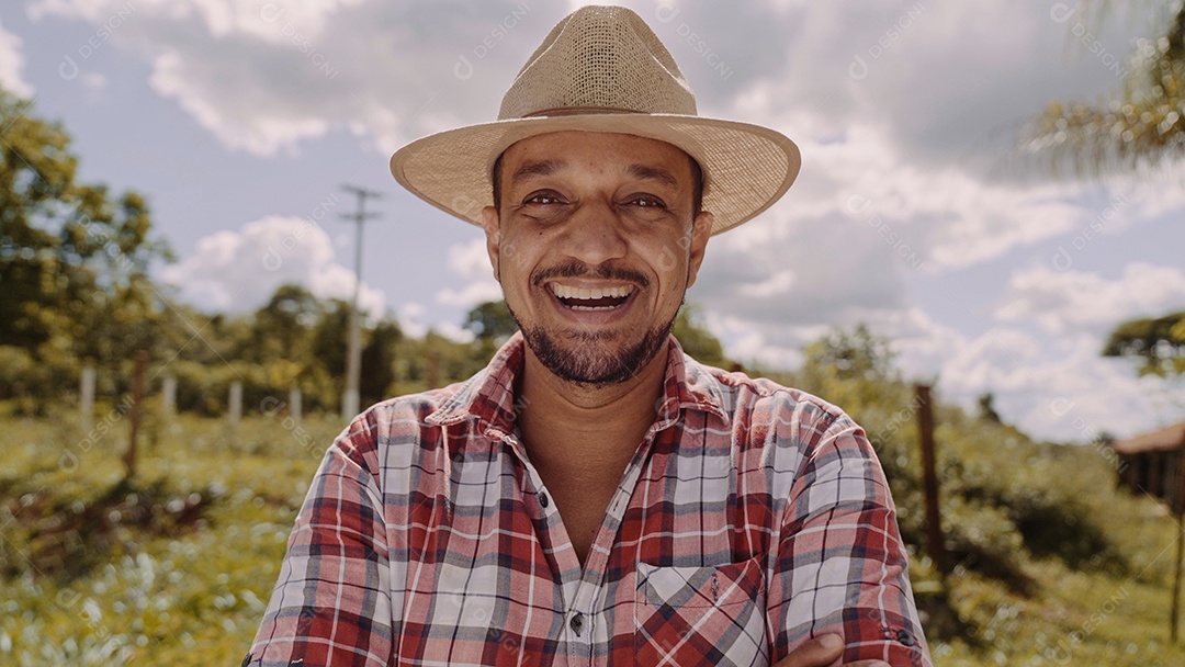 Retrato de jovem agricultor com mãos cruzadas na camisa casual e chapéu na fazenda