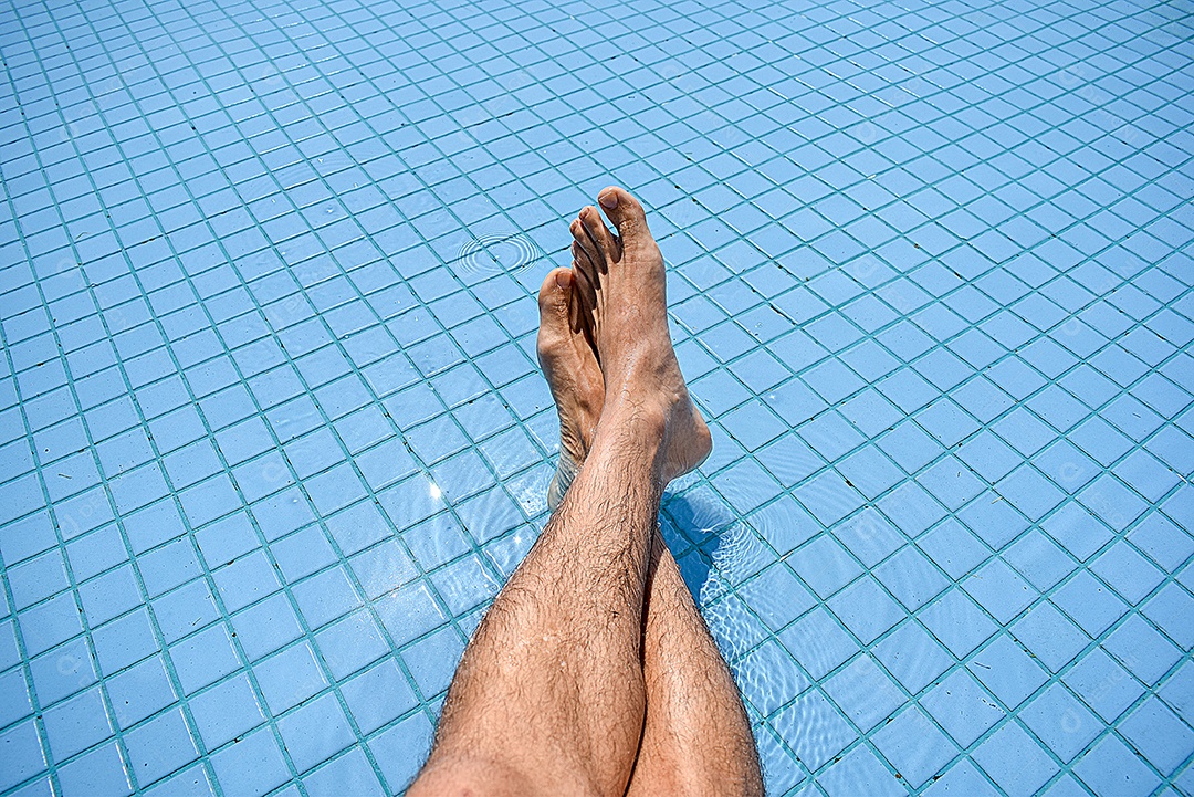 Homem relaxando na piscina com as pernas cruzadas em um dia ensolarado.