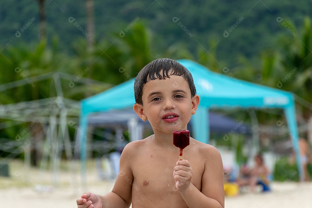 Criança com picolé de morango na praia derretendo na mão