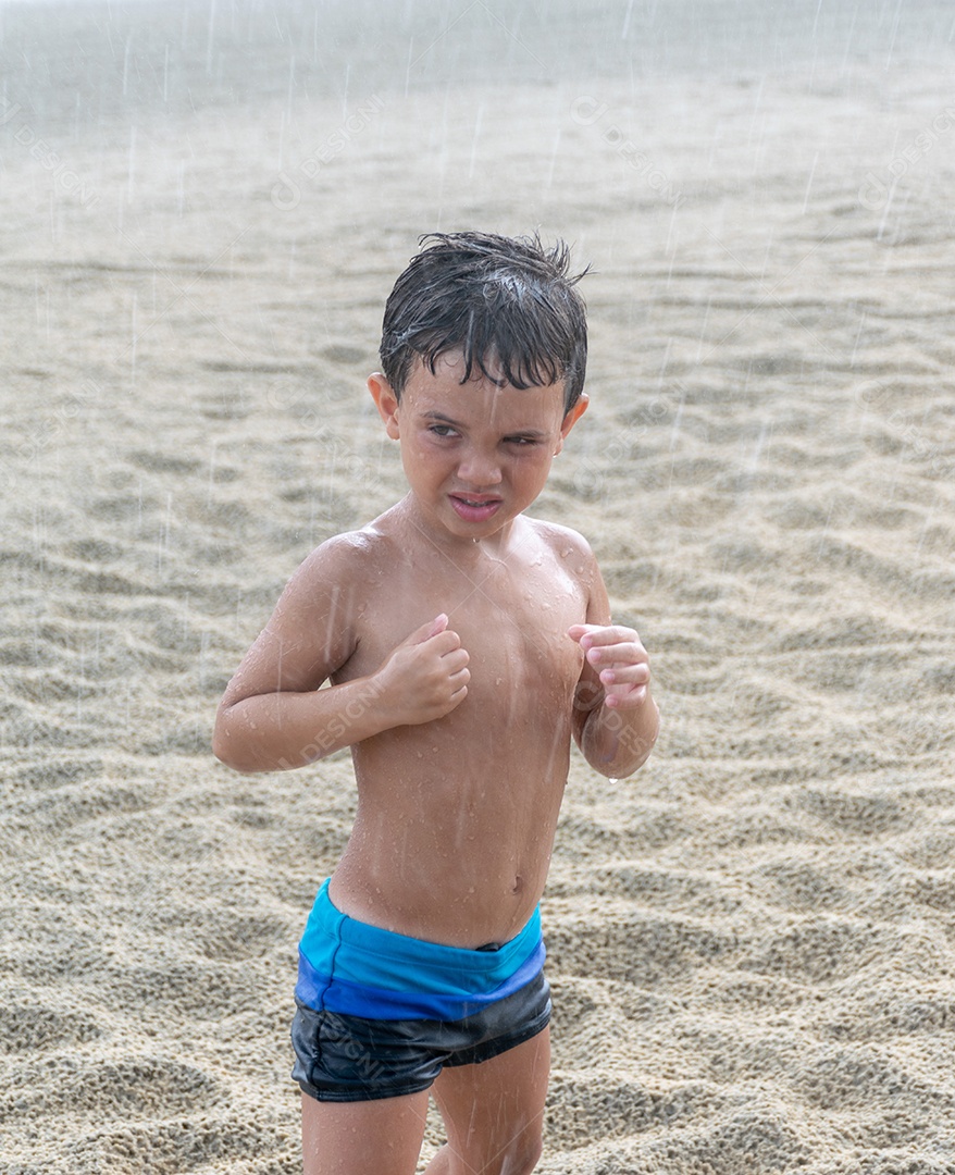 Criança sorrindo na chuva na areia da praia