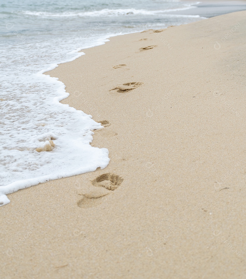 Pegadas humanas na areia da praia mar ao fundo.