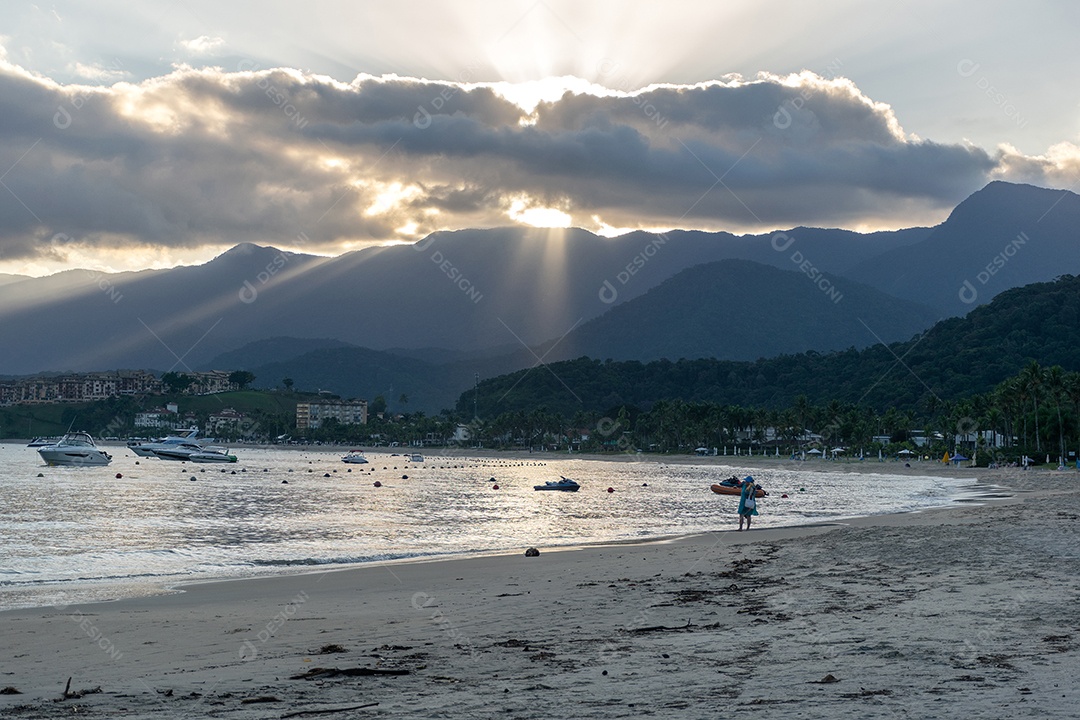 Pôr do sol na praia, entre as nuvens e atrás do morro