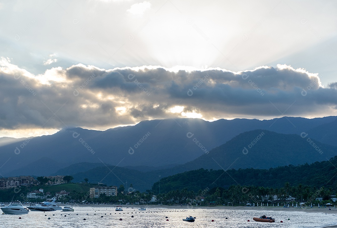 Pôr do sol na praia, entre as nuvens e atrás do morro