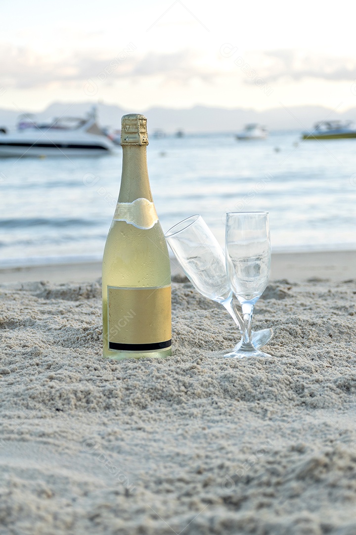 Garrafa de champanhe e duas taças na areia da praia