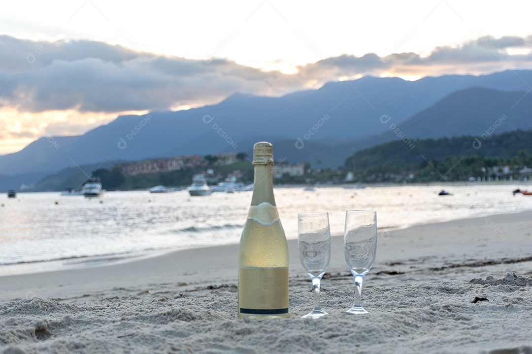 Garrafa de champanhe e duas taças na areia da praia