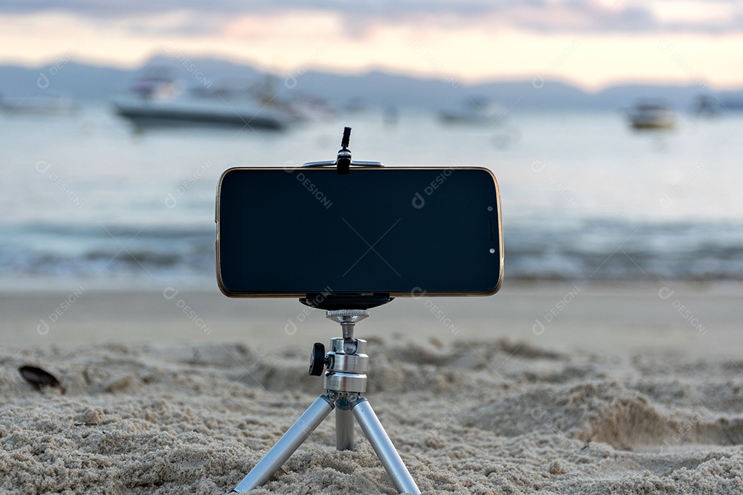 Celular preso em tripé tirando foto do pôr do sol na praia lente em 18mm .