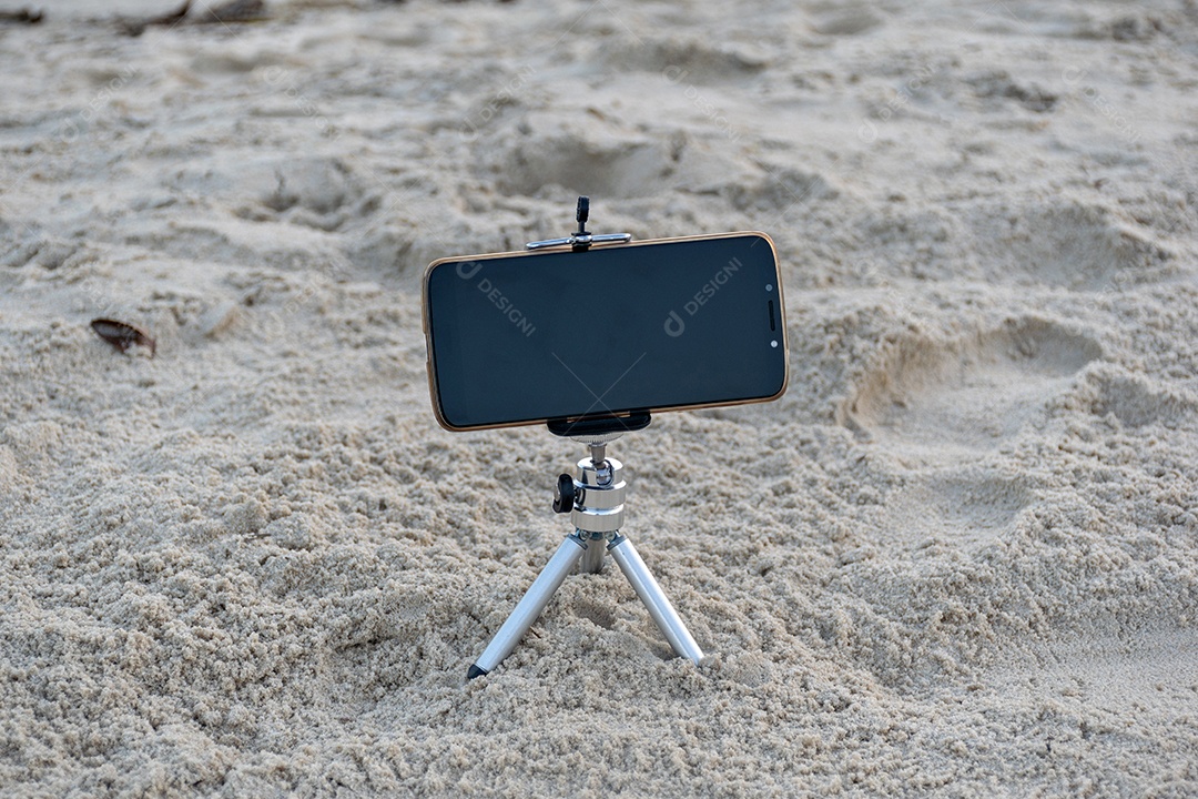 Celular preso em tripé tirando foto do pôr do sol na praia lente em 18mm .