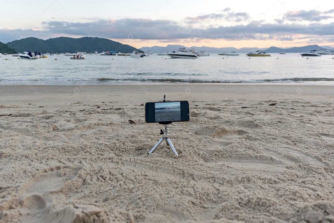 Celular preso em tripé tirando foto do pôr do sol na praia lente em 18mm .