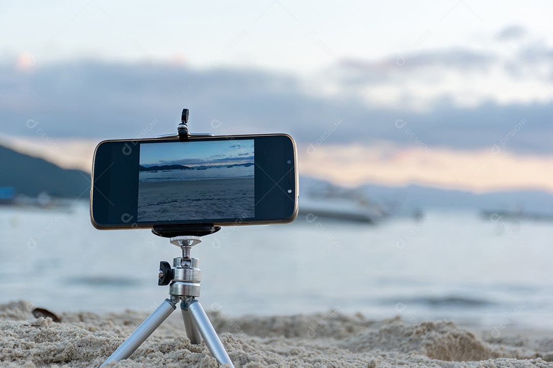 Celular preso em tripé tirando foto do pôr do sol na praia lente em 18mm .