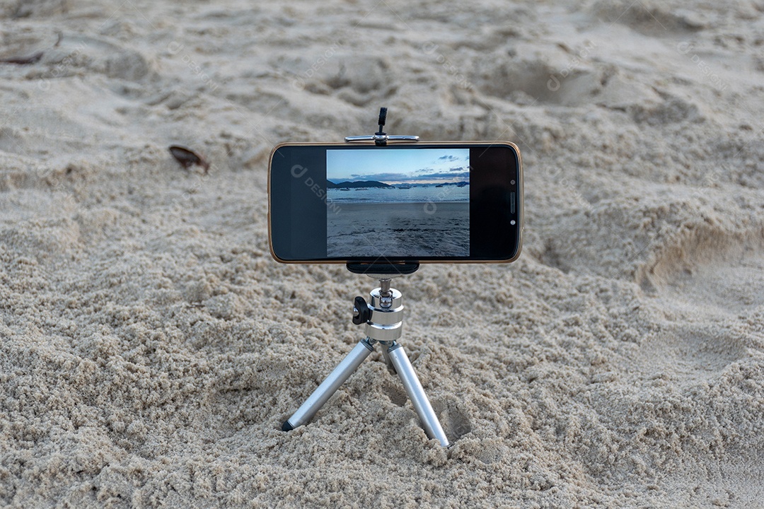 Celular preso em tripé tirando foto do pôr do sol na praia lente em 18mm .
