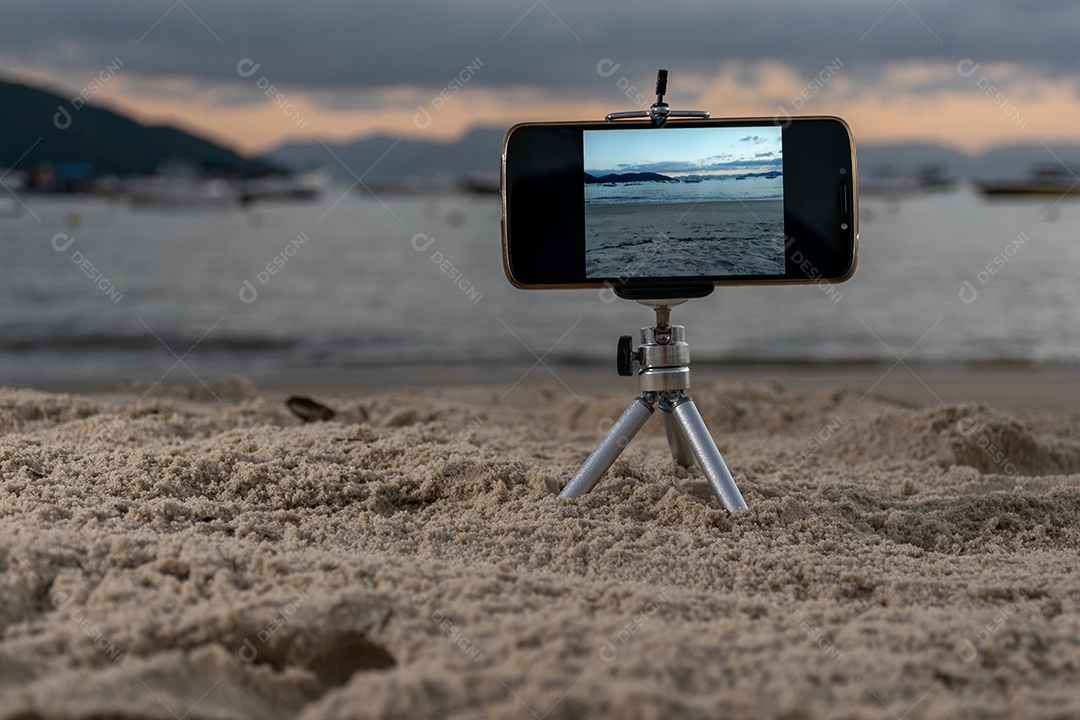 Celular preso em tripé tirando foto do pôr do sol na praia lente em 18mm .