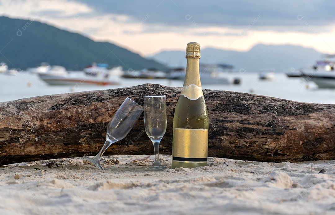 Garrafa de champanhe e duas taças na areia da praiac