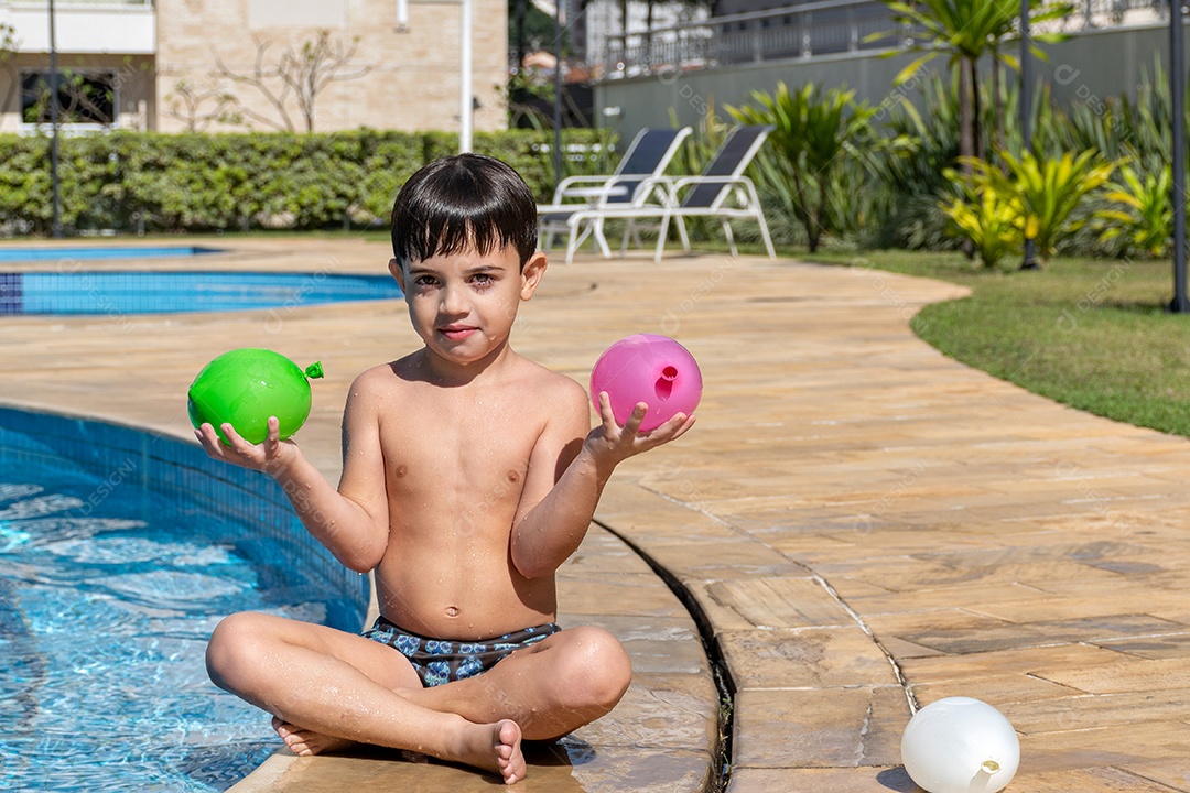 Menino em frente à piscina brincando com um balão de água.