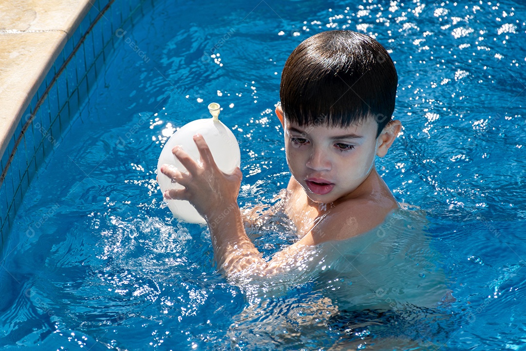 Menino dentro da piscina pronto para jogar um balão de água.