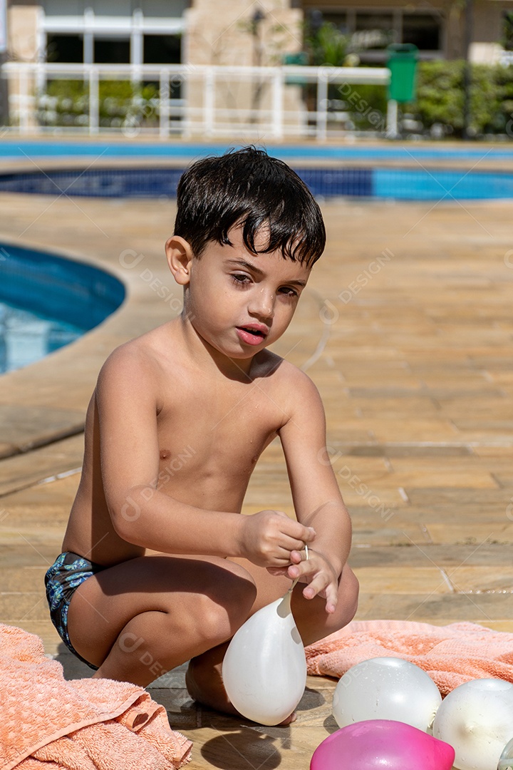 Menino em frente à piscina brincando com um balão de água.