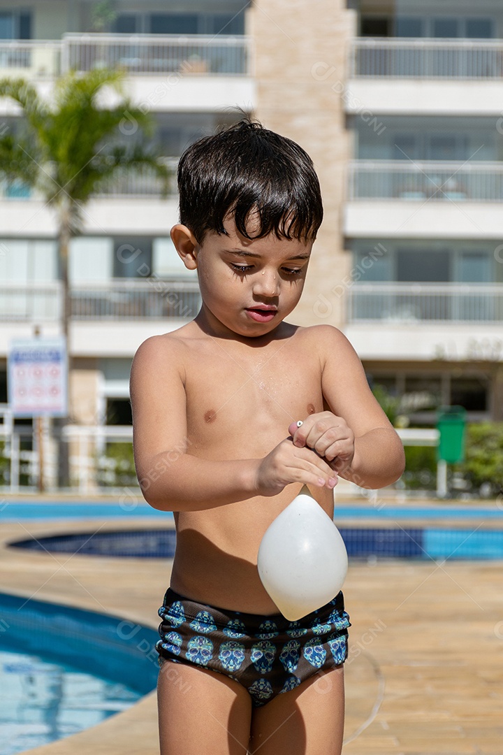 Menino em frente à piscina brincando com um balão de água.