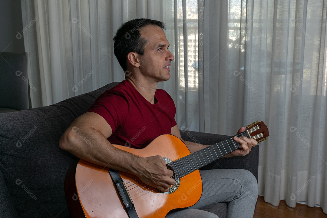 Homem maduro 44 anos sentado no chão e interagindo com um violão e um copo de cerveja.