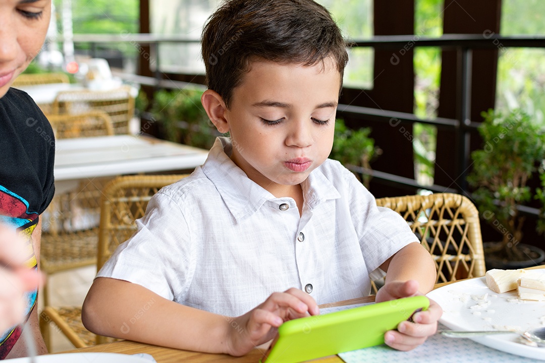 Menino de 6 anos mexendo em seu celular em restaurante.