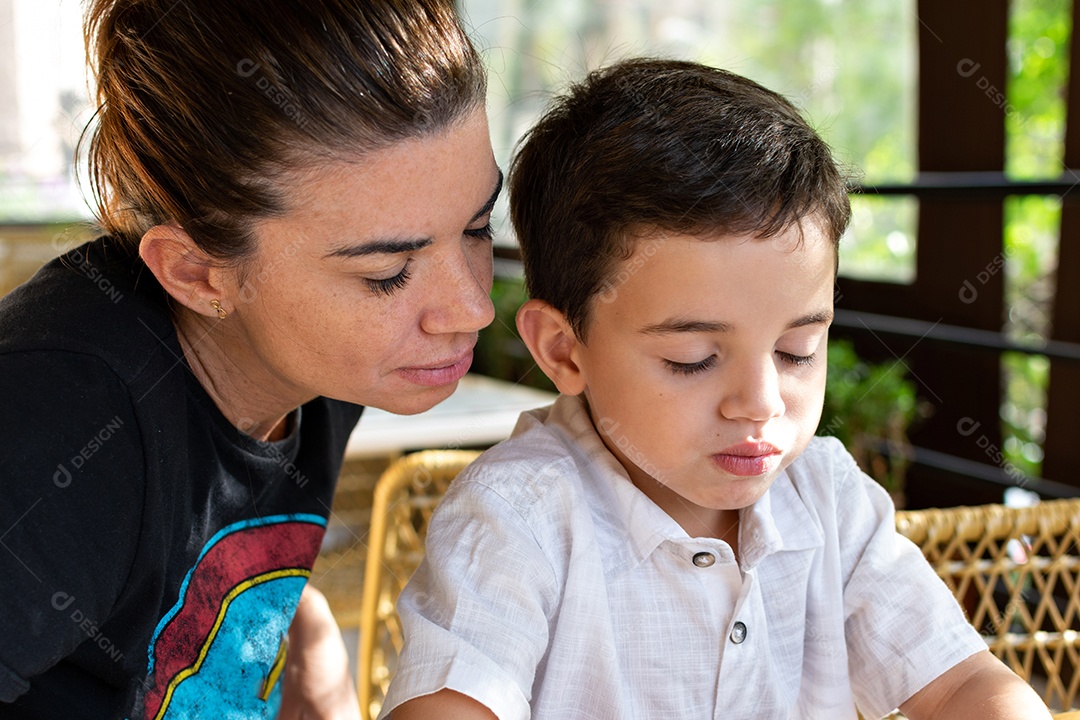 Mãe e filho olhando para o celular na mesa.