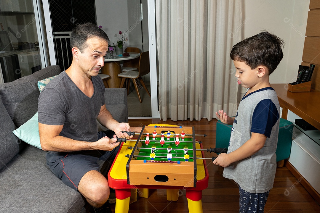 Pai e filho jogando mini pebolim em casa.