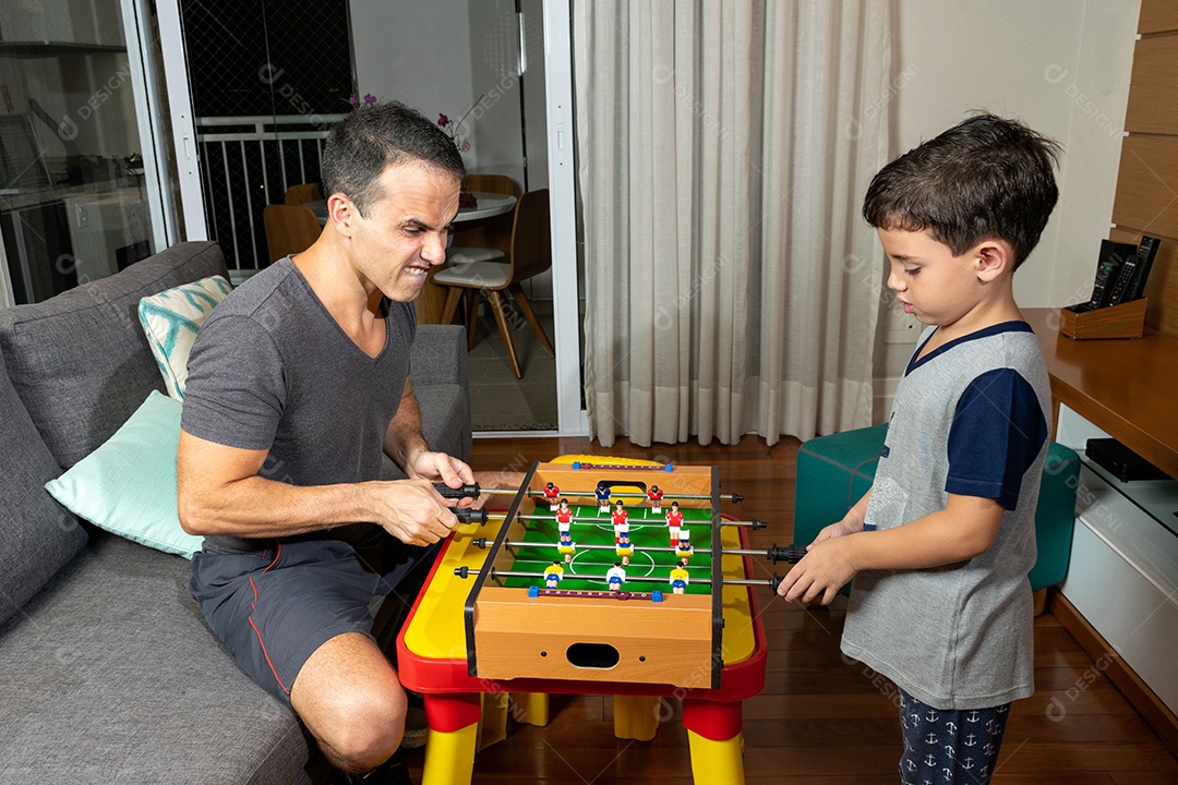 Pai e filho jogando mini pebolim em casa.
