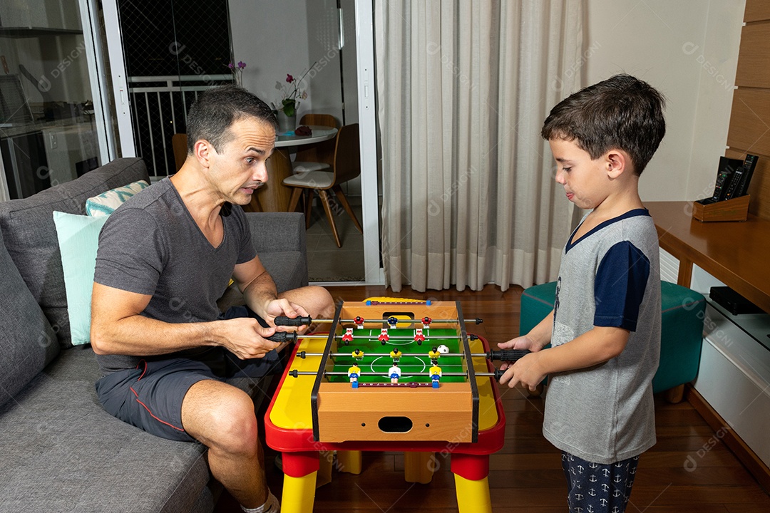 Pai e filho jogando mini pebolim em casa.