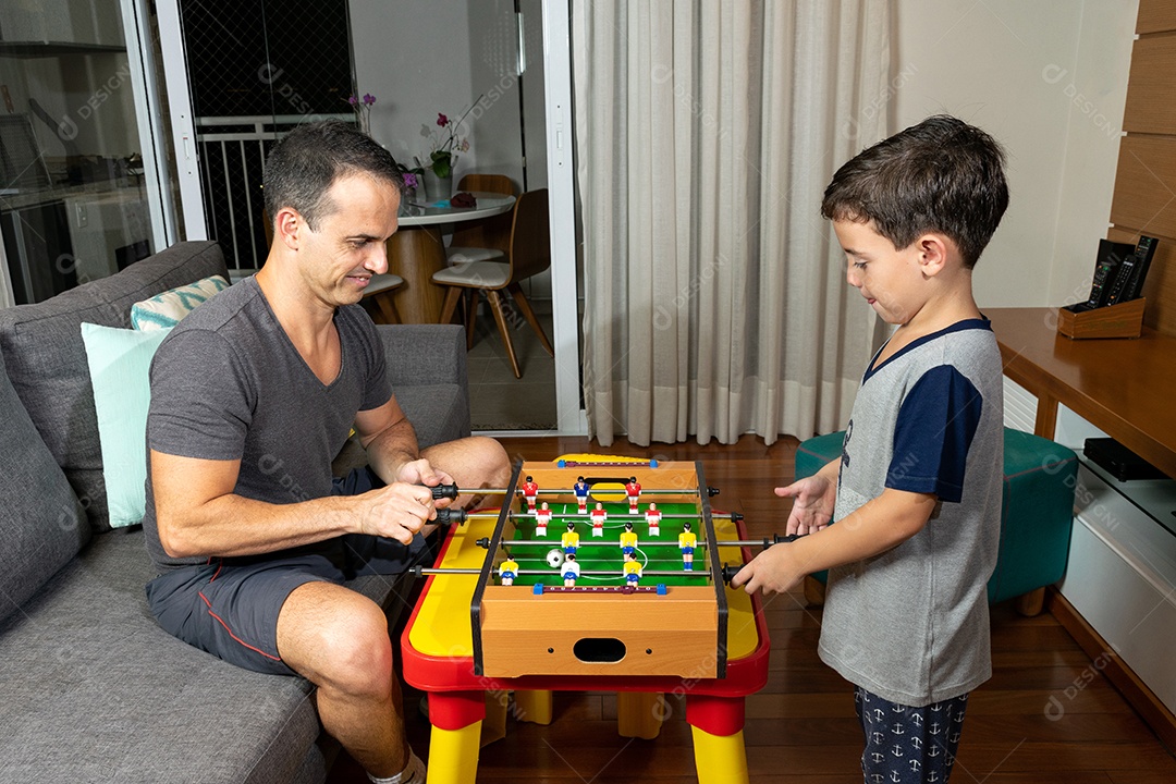 Pai e filho jogando mini pebolim em casa.