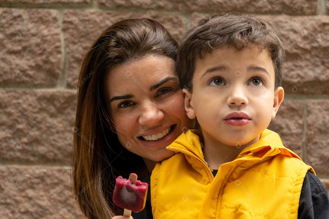 Mãe sorridente atrás de seu filho segurando um picolé com colete amarelo