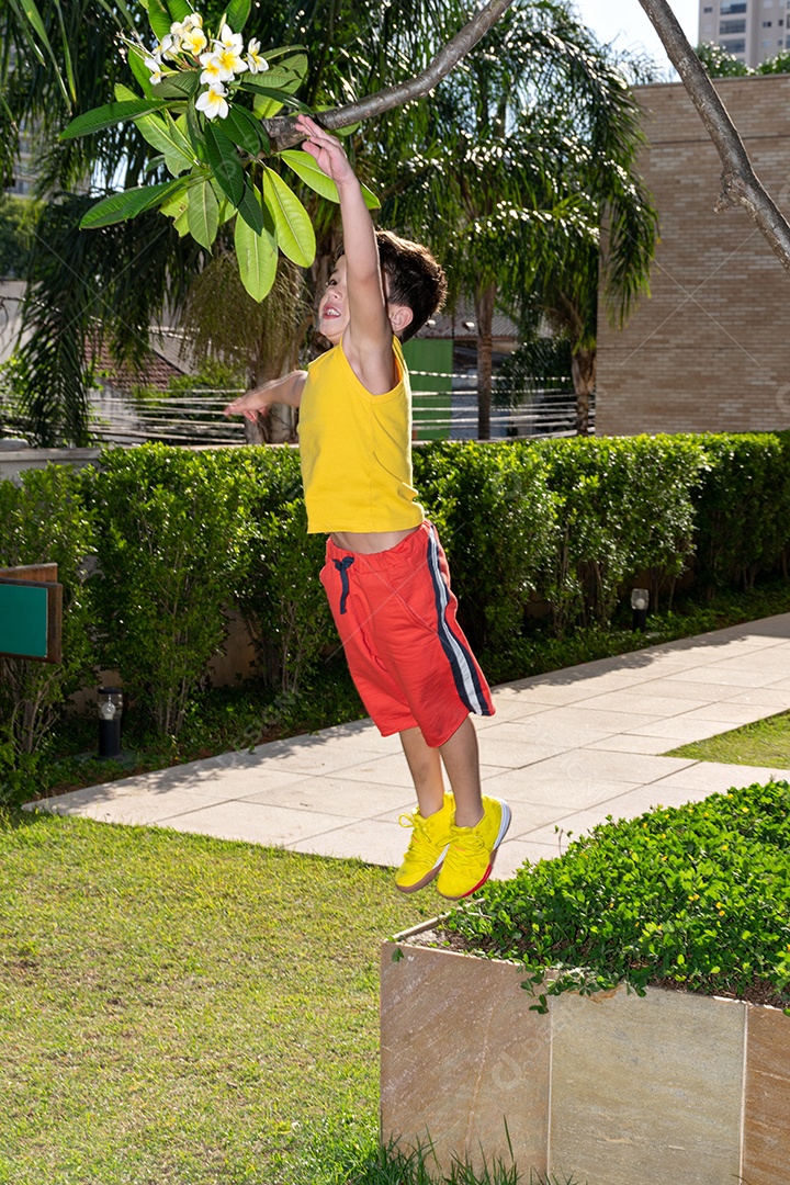 Menino de 6 anos pulando e pegando uma flor branca.