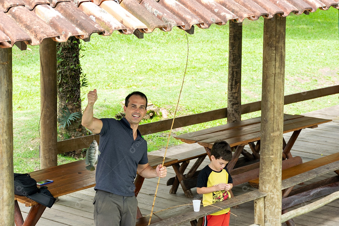 Homem ao lado de seu filho pescando, feliz e surpreso por ter pego um peixe