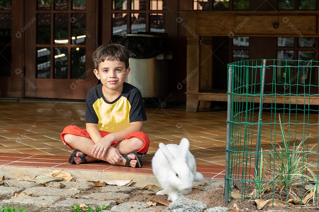 Criança acariciando sentado ao lado de um coelho nas férias de verão.