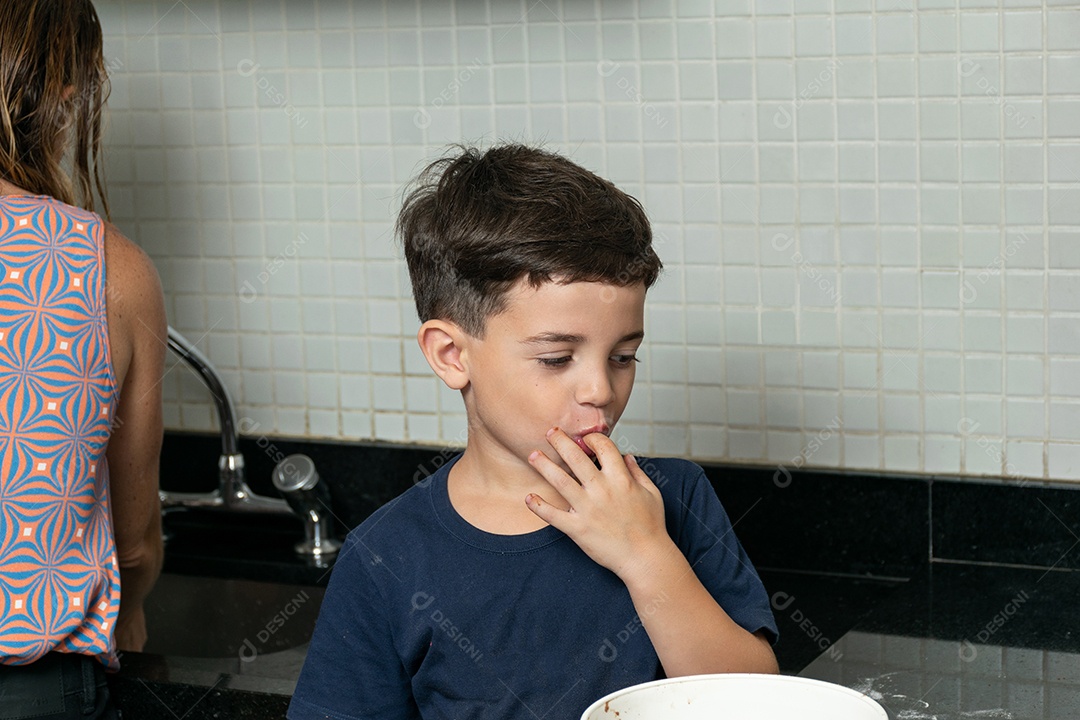 Garoto ajudando a mãe a fazer biscoitos e lambendo o dedo.