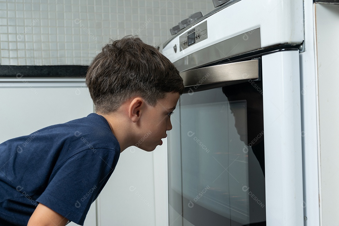 Menino esperando em frente ao fogão os biscoitos serem assados.