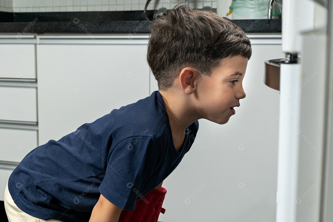 Menino esperando em frente ao fogão os biscoitos serem assados.