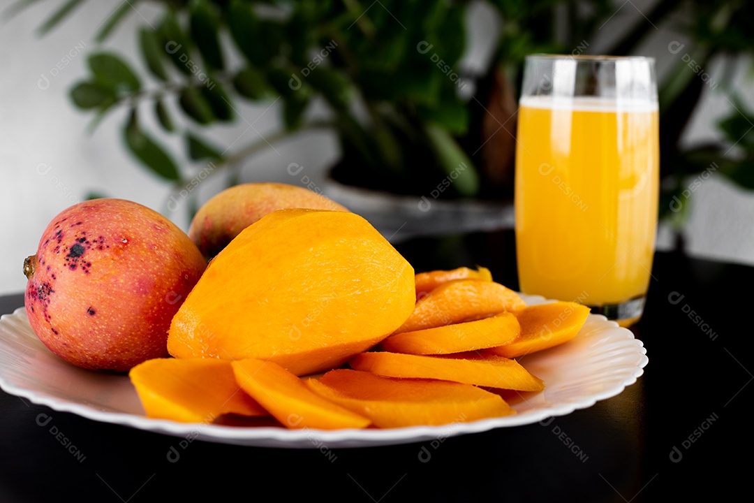 Prato de comida com pedaços manga fatiada copo de suco ao lado