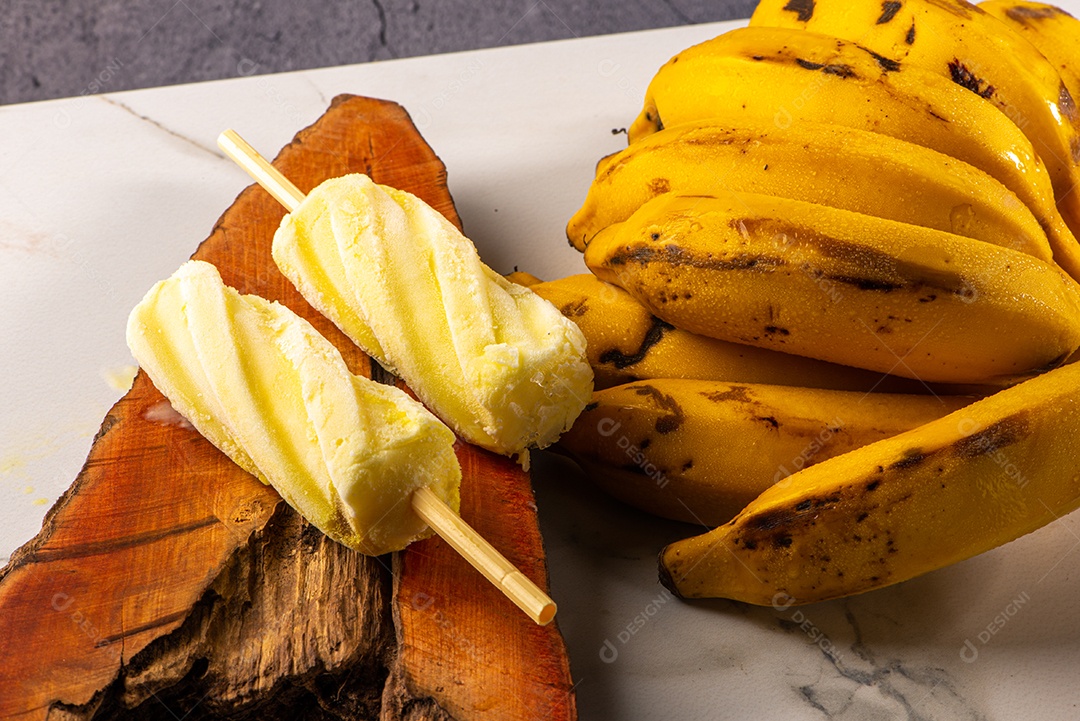 Sorvete de banana apoiado em cacho de banana em fundo branco.