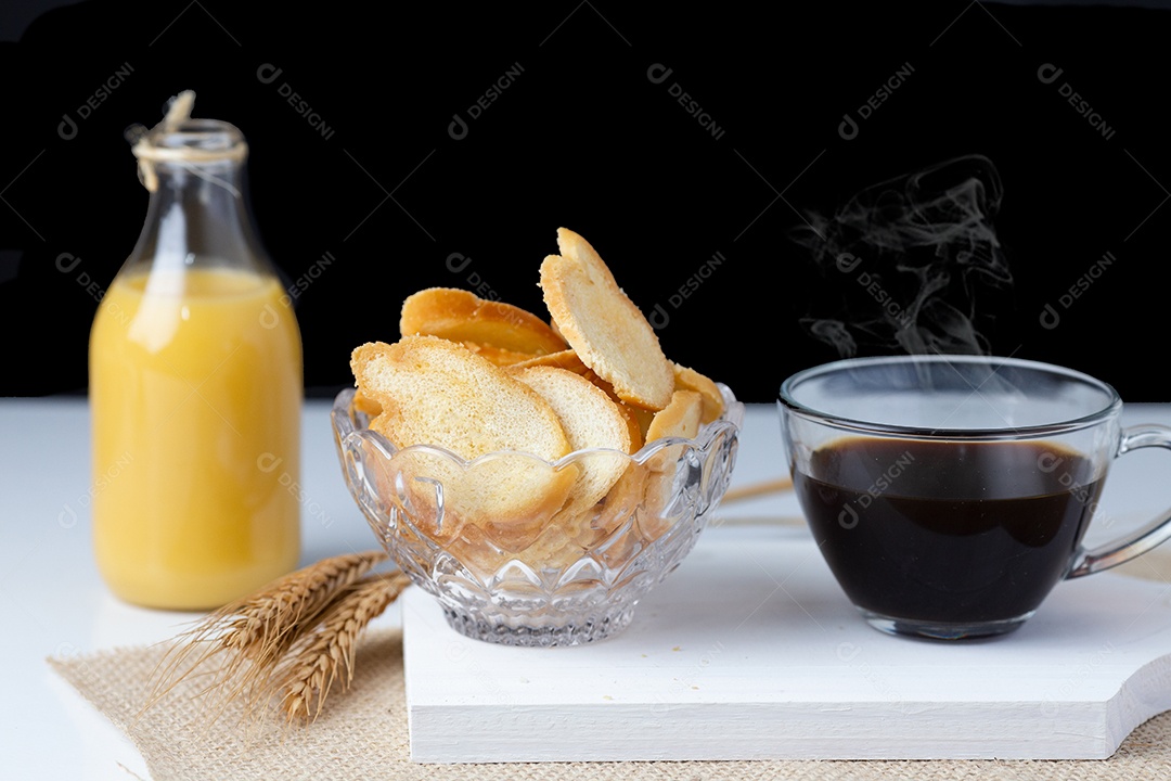 Pães sobre uma tigela ao lado de jarra de suco xicara café  tabua de madeira