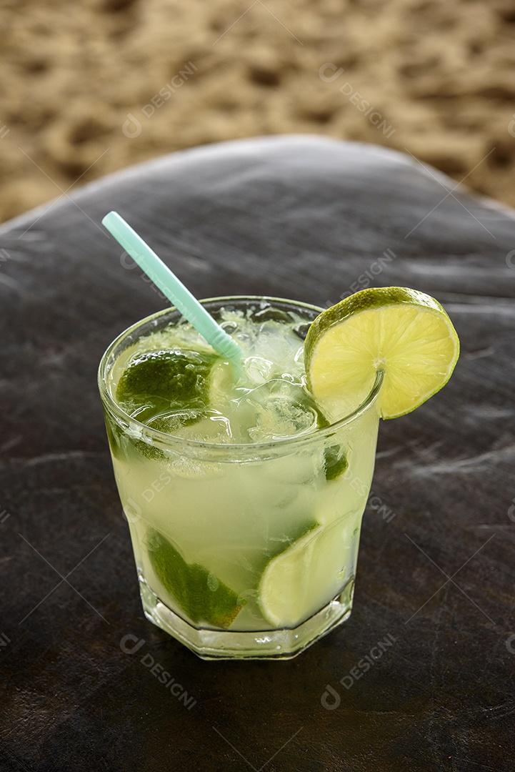 Bebida caipirinha brasileira na mesa de madeira com fundo de praia.