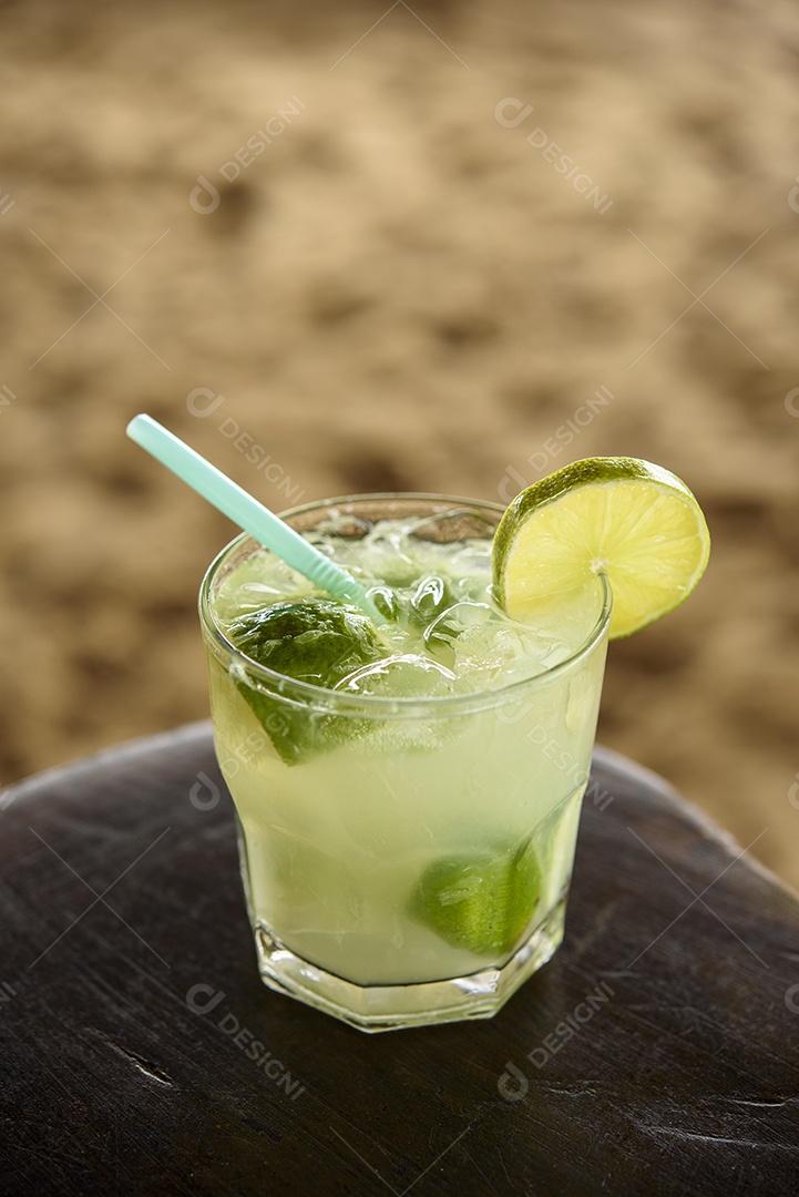 Bebida caipirinha brasileira na mesa de madeira com fundo de praia.