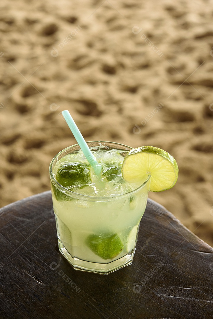 Bebida caipirinha brasileira na mesa de madeira com fundo de praia.