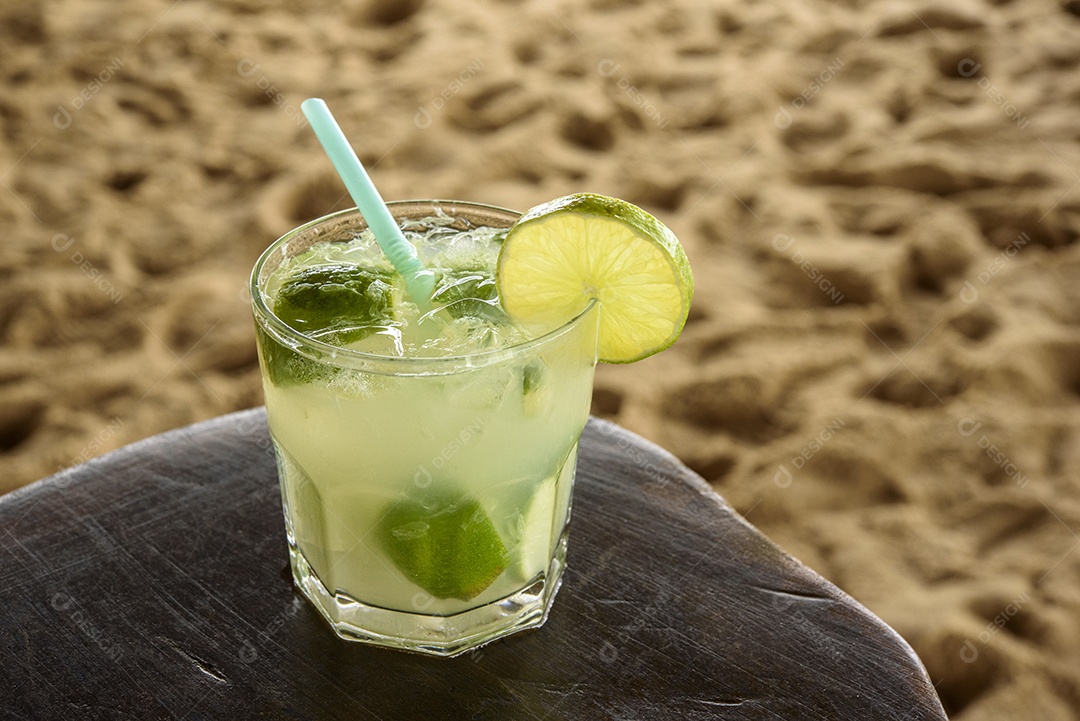Bebida caipirinha brasileira na mesa de madeira com fundo de praia.